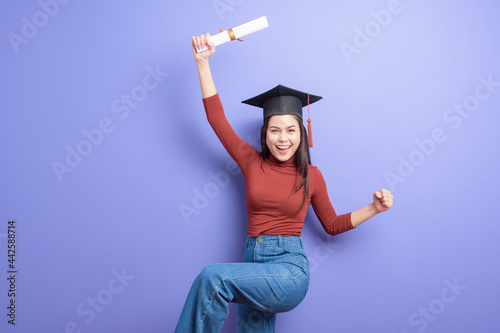 Portrait of young University student woman with graduation cap on violet background photo