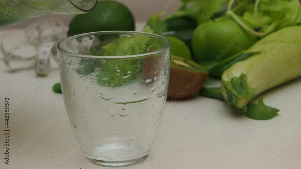 woman cuts green fruits and vegetables to blending spinach, cucumber, ice to make a healthy green smoothie. Woman pouring a green detox juice from blender to a glass woman cuts green fruits and vegetables to blending spinach, cucumber, ice to make a healthy green smoothie. Woman pouring a green detox juice from blender to a glass
