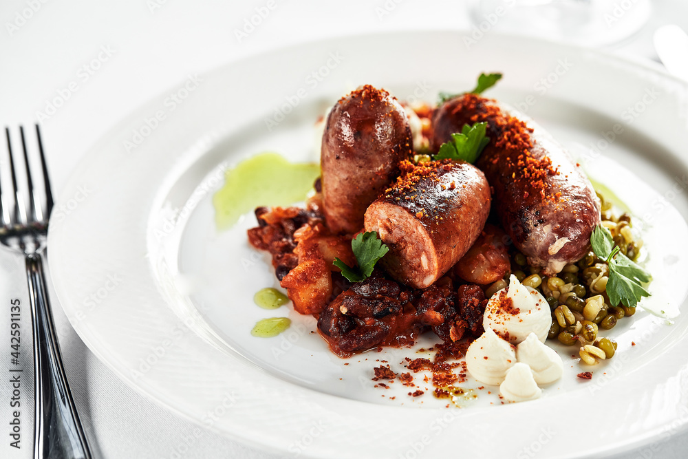 Grilled sausages sauce on a white plate with herbs, on a festive table, light background, copy space Grilled sausages sauce on a white plate with herbs, on a festive table, light background, copy space