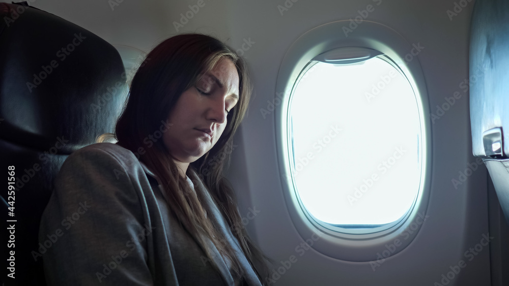 Fototapeta premium Brunette woman sleeping while sitting in an uncomfortable position on the plane.