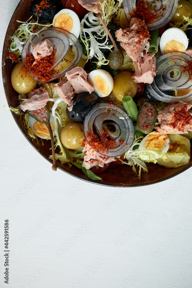 Classic nicoise in the author's serving tuna salad with fresh vegetables on a white napkin, canned tuna with masilnas, onions and eggs, top view, copy space