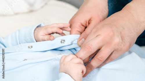 CLoseup of mother s hands unbuttoning and changing clothes of her little baby son. Concept of parent baby hygiene and child development