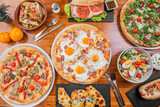 Assorted pizza prepared in an Argentine restaurant. Pizza with fried eggs, caesar salad, pizza with arugula and ham, empanadas, hot dog.