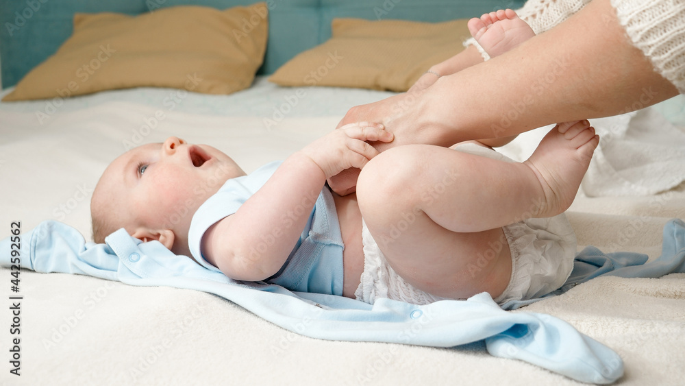 Cute little baby boy looking at mother while she is changing his messy diapers on bed. Concept of parenting ,baby hygiene and child development.