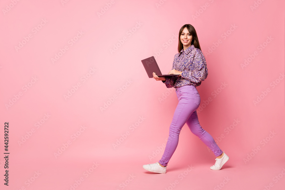 Full length profile photo of cheerful charming person walking hands hold laptop isolated on pink color background Full length profile photo of cheerful charming person walking hands hold laptop isolated on pink color background