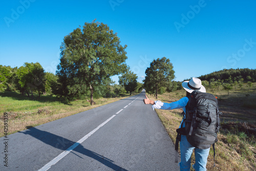 Young woman with backpack travelling by car. Hitchhiking on the road. Traveling by autostop. Backpacker stopping car with thumbs up. Way to adventure. Budget or cheap travel.