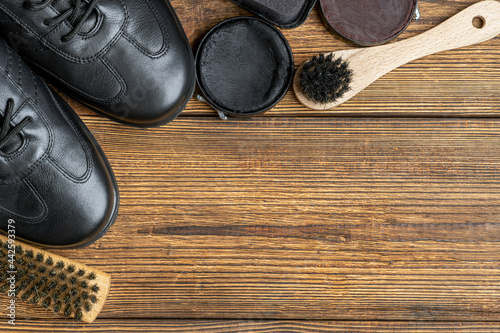 leather boots, brushes, shoe polish wax, footwear care products on wooden background with copy space