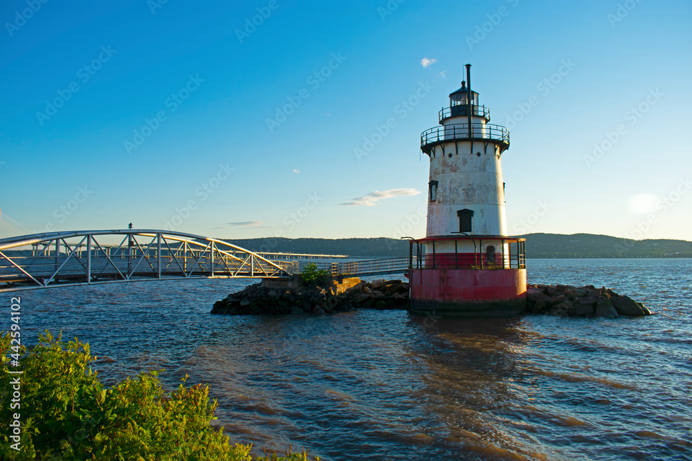 Short, red and white lighthouse on the Hudson River with a small bridge leading to it and a larger bridge further in the background -05