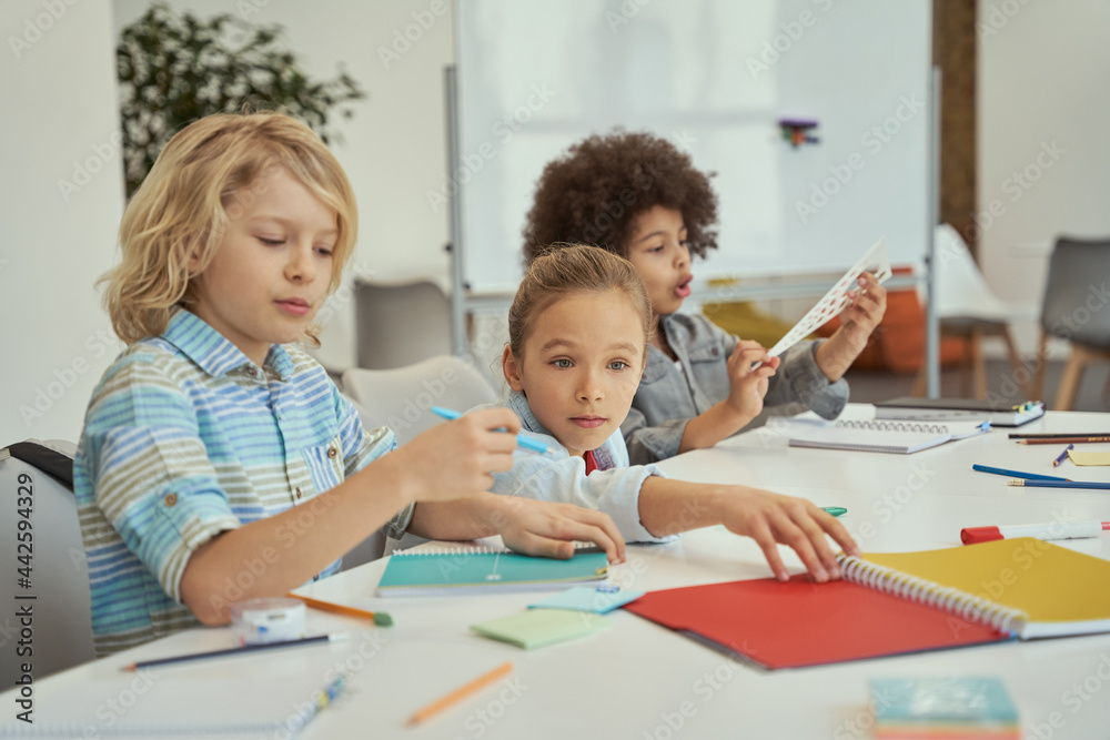 Social activity. Diverse kids sitting together at the table in elementary school classroom Social activity. Diverse kids sitting together at the table in elementary school classroom