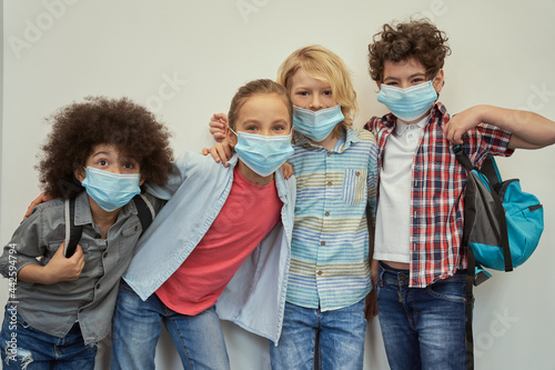 We are a team. Four cute multinational kids wearing protective face masks smiling at camera, posing together over light background