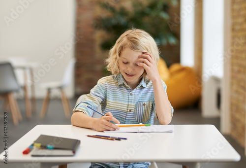 Solve equation. Diligent elementary school boy doing sums, writing in his notebook while sitting at the desk in classroom
