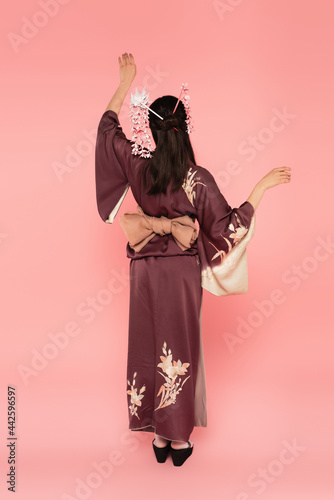 Back view of woman in kimono and kanzashi standing on pink background photo