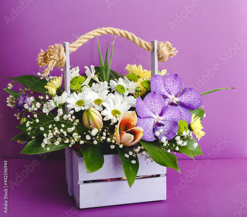 Beautiful bouquet of flowers in lilac wooden basket on purple color background. Floral visuals Floral floristic blooming composition.
