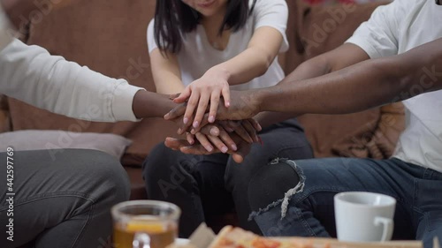 Handstack of unrecognizable African American men and Asian woman. Group of friends meeting indoors sitting on comfortable couch stacking hands