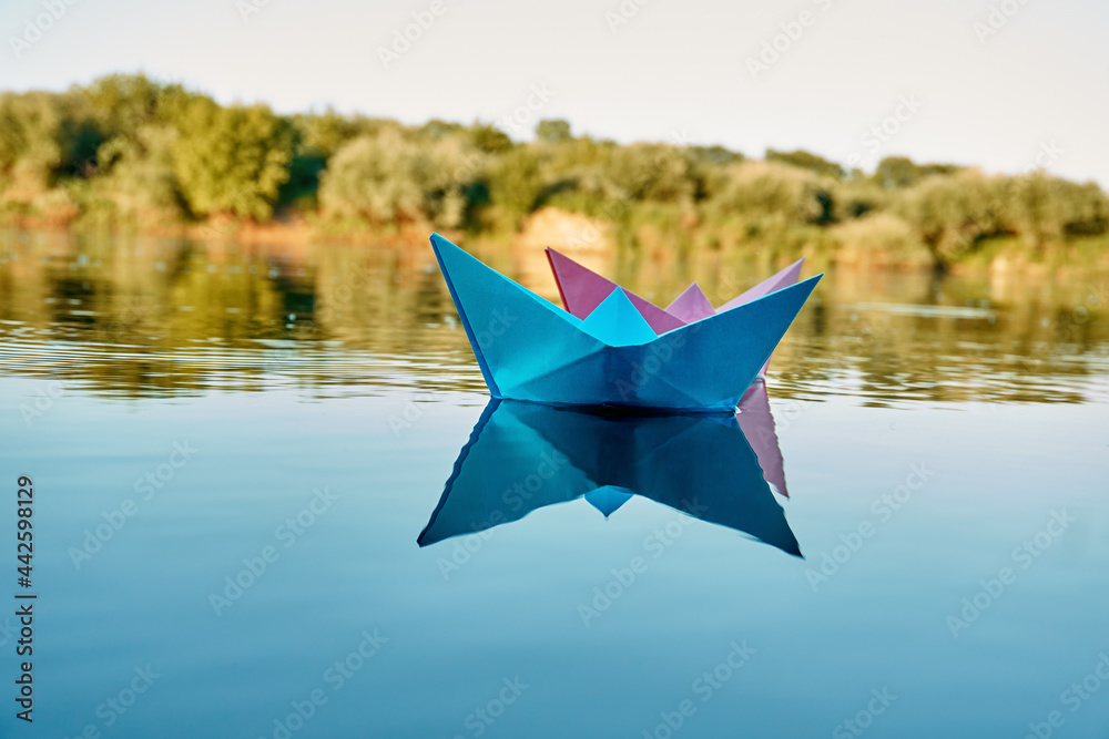 Two blue and pink boats sail in a pond, a river. In the background are bushes and trees