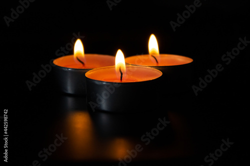 Dark night background, composition of three candles. Black table, side view. Candles Burning at Night. Orange taper burning in focus, foreground. illustration design.