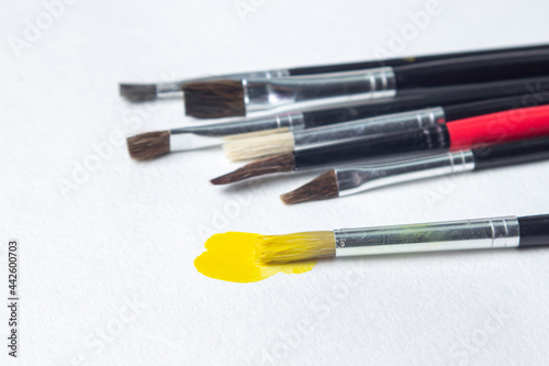 Paint brushes on a white background. One brush with yellow paint. Watercolor paint