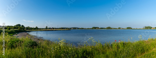 panorama landscape of a small ocean lagoon with a sandy beach and a wildflower meadow under a blue sky