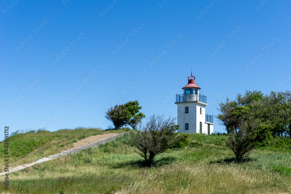 view of the Hundested lighthouse on ist grassy hill under a blue sky