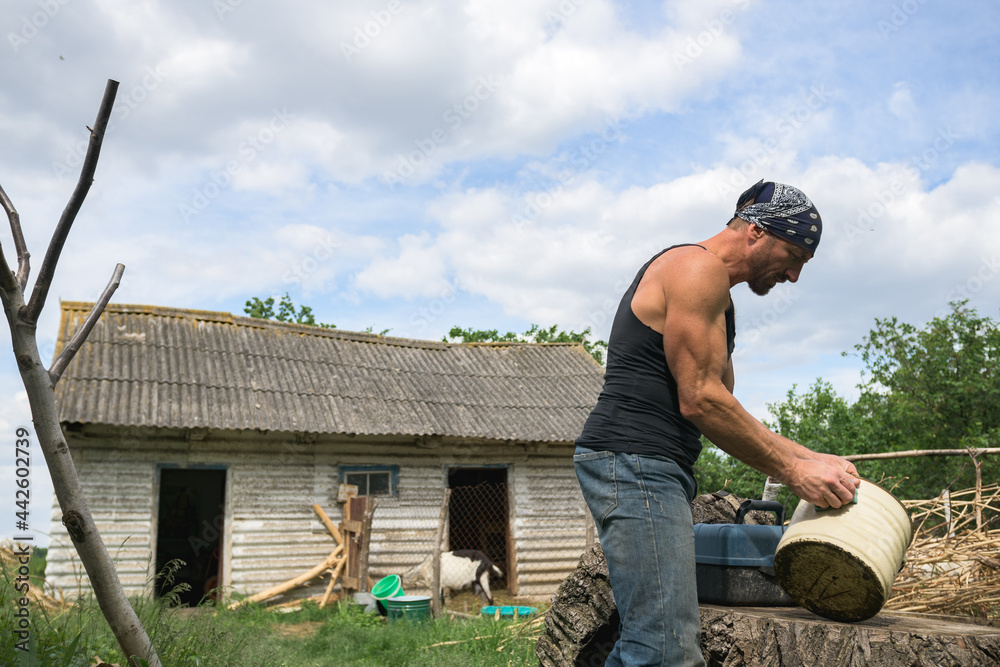 Side view of muscular farmer in bandana holding bucket on ranch Stock
