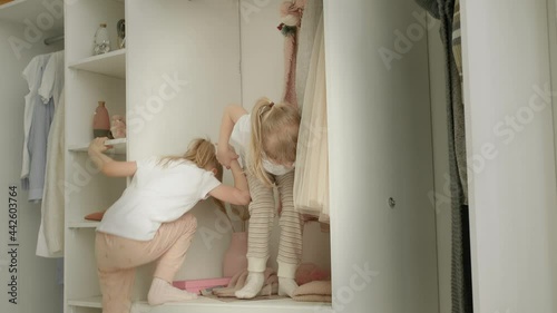 girl helping her sister to climb on the shelf of the closet