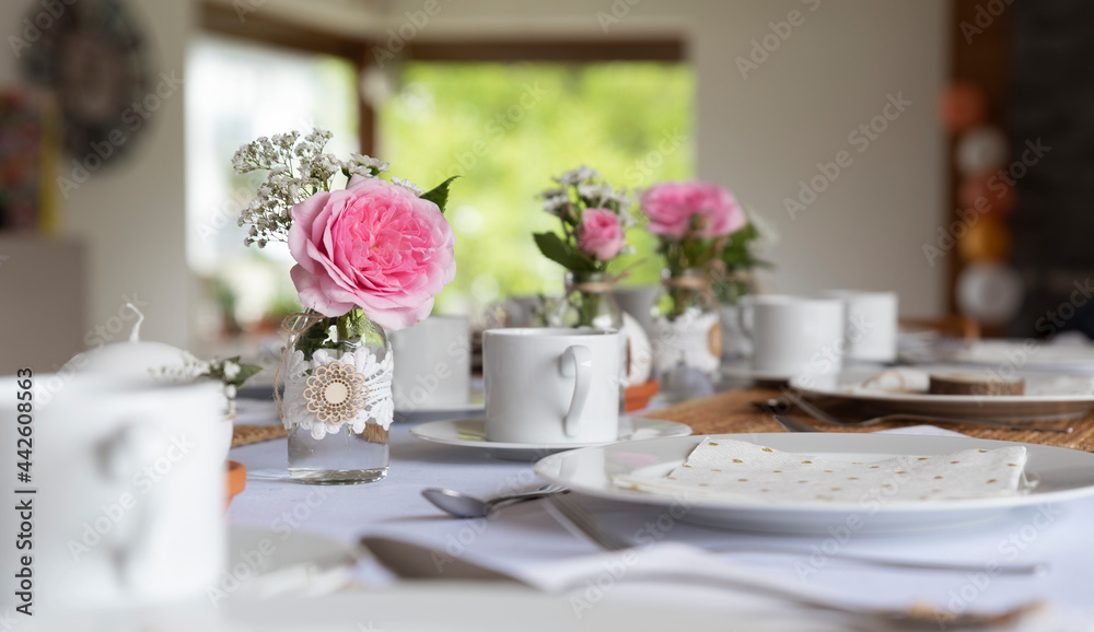 Wedding table setting with flowers, white tableware and pink fresh flowers. Party and catering in nice interior with window. Dining room with natural plants.