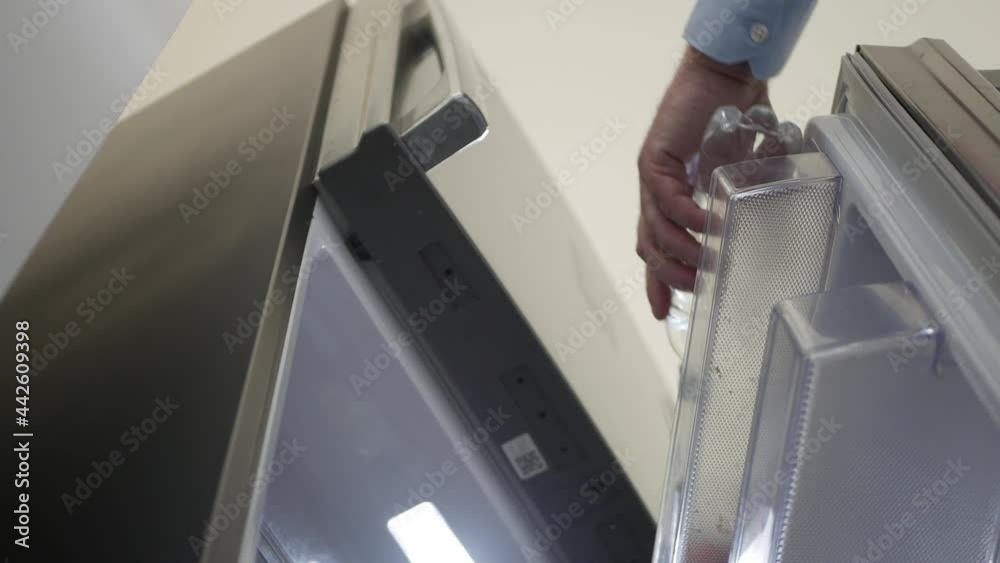 Thirsty Person Opens the Door Fridge and Put Inside a Bottle with Fresh Water. Thirsty Person Opens the Door Fridge and Put Inside a Bottle with Fresh Water.