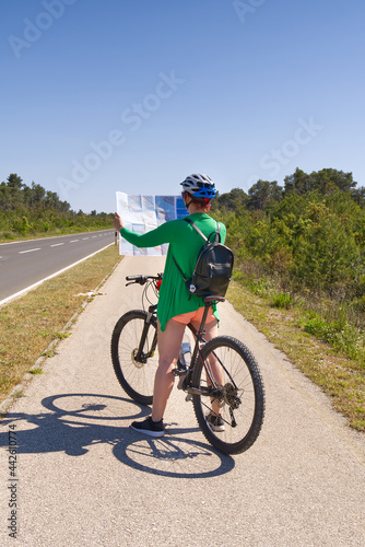 tourist, happy woman in a helmet on a bicycle examining a map at the intersection of bicycle roads. concept of outdoor activities or cycling travel in sunny day