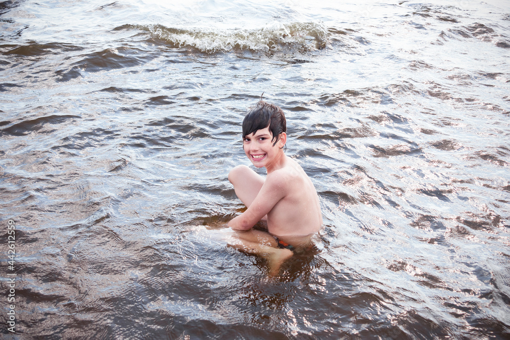 Fototapeta premium Smiling boy sitting in the water among the waves.