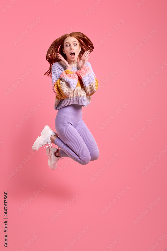Shocked lady jump high celebrate black friday sales shopping center opening, in casual sweater and leggins, isolated over pink color background. Woman in shock by discounts in shop. Copy space