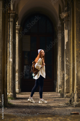 Redhead Tourist female travel destination visiting abandoned old place on vacation. Beautiful woman walking on summer holidays, cold weather outdoors. Woman is dressed in coat and hat © alfa27