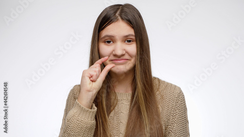 Bilde på lerret Smiling portrait of girl showing small or tiny gesture over white studio background