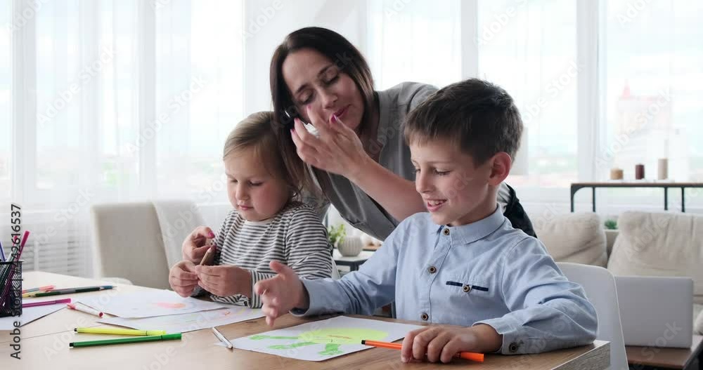 Mother helping little daughter and son drawing on paper at home