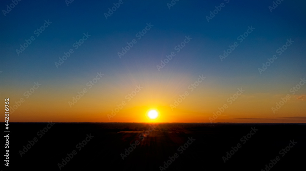 Summer sunset in clear sky. Sun goes down to horizon. Black foreground