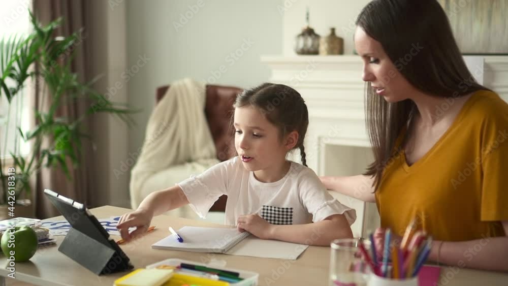 Girl make homework using tablet online with mother helping Spbd. Primary school child study with mom Girl make homework using tablet online with mother helping Spbd. Primary school child study with mom