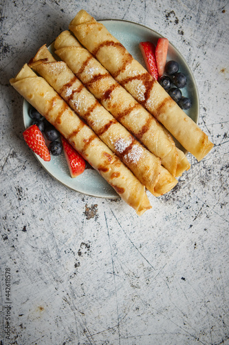 Plate of delicious crepes roll with fresh fruits and chocolate