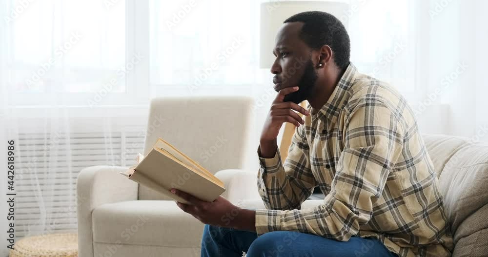 Thoughtful man reading book on sofa at home