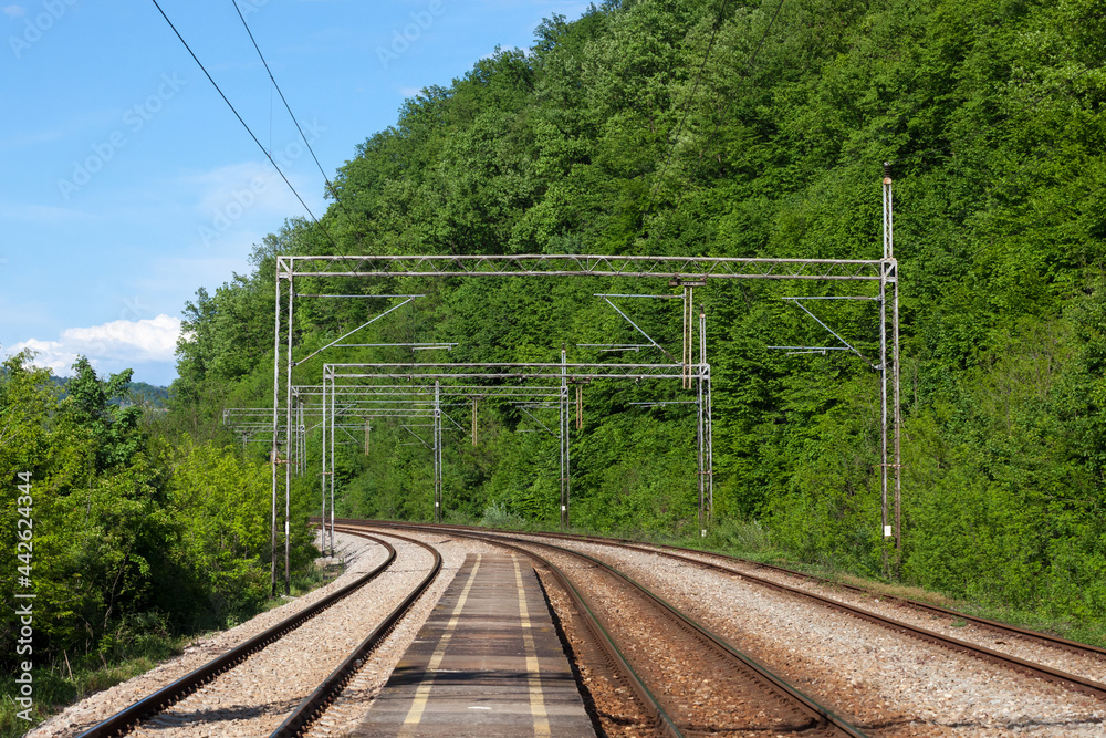 Railway tracks, rails and platforms in a train station in a middle of a forest in Serbia, electrified, with power overhead line, on a double track main railroad line... Railway tracks, rails and platforms in a train station in a middle of a forest in Serbia, electrified, with power overhead line, on a double track main railroad line...