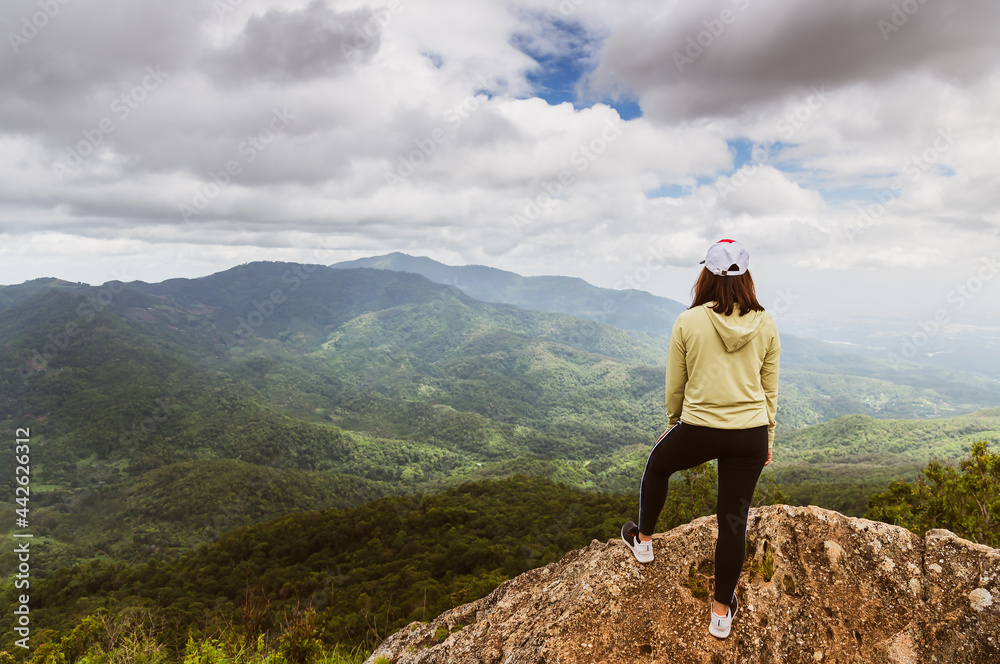 Asian woman in sportswear standing on mountain peak with mountain and forest background in cloudy sky active outdoor exercising lifestyle.