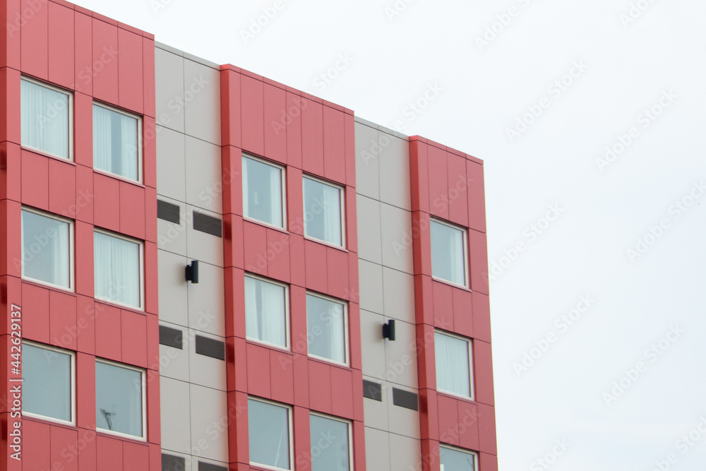 Commercial external metal composite panels on a building with blue sky and clouds in the background. The durable metal composite panels are both red and grey in colour on the modern building.