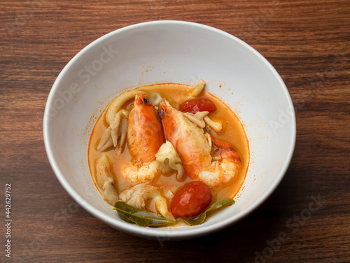 hot and spicy shrimp soup (Thai food Tom Yum Goong) in white bowl on wooden table, homemade cooking, boiled prawn with herbs