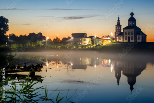 Beautiful evening sunset of a small town reflected in the lake. Night fog over the lake.