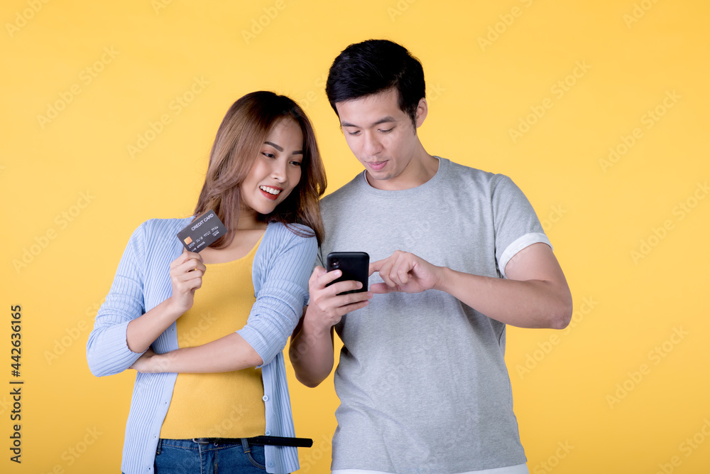 Asian couple holding credit card and smartphone isolated on yellow background Asian couple holding credit card and smartphone isolated on yellow background