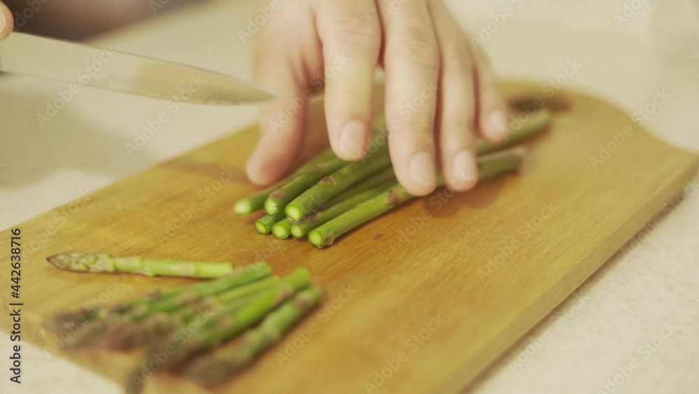 Chopping raw green asparagus before cooking on a wooden board Chopping raw green asparagus before cooking on a wooden board