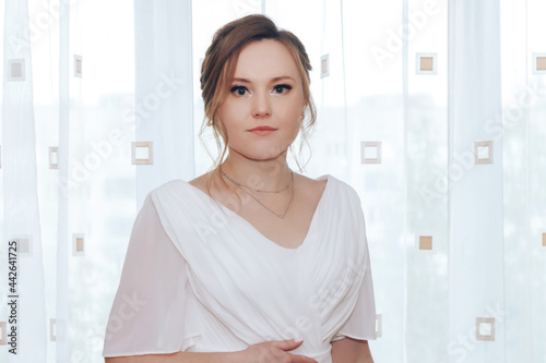 Free Download Portrait of a beautiful young bride in a white elegant wedding dress, standing at the window - GFXLoad