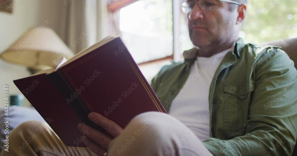 Caucasian man sitting on sofa, reading book at home