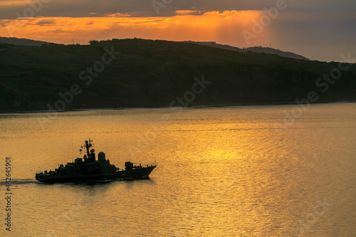 A Russian military ship is sailing during a bright dawn. Silhouette of a Russian military ship in Vladivostok.