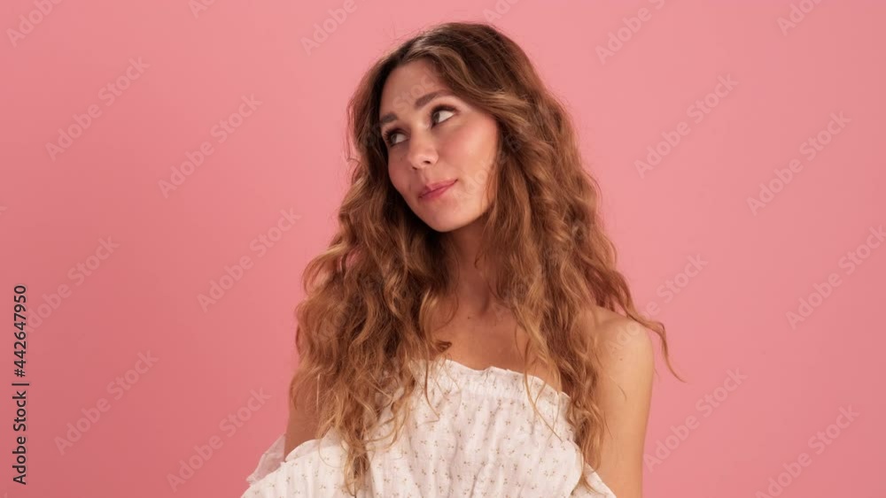 A shy woman in a lace dress sending an air kiss at the camera in the pink studio 