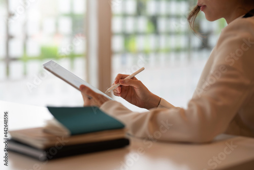 Close-up of a businesswoman holding a pen to taking notes on a tablet at the office.