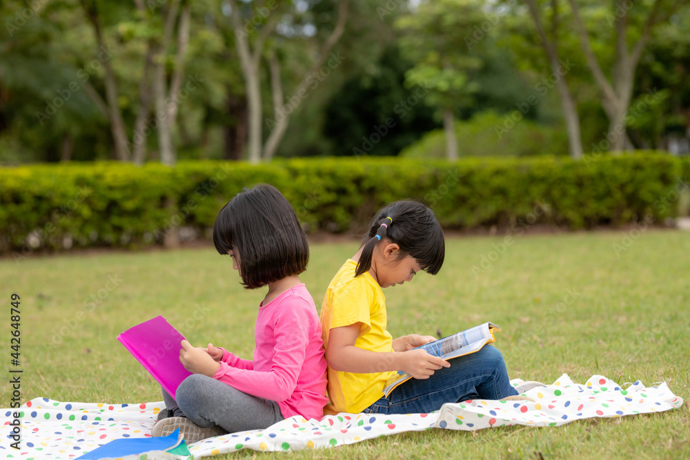 two beautiful little girls reading books in the garden , sitting on grass. The concept of education and friendship.